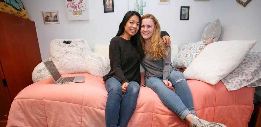 two female students sitting on dorm room bed